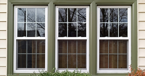 Three white-framed, double-hung windows with grid patterns, set into a wall with olive green trim and beige siding.