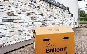 A box of Belterra stone veneer sits on a driveway next to a wall finished with the matching white and gray stacked stone.