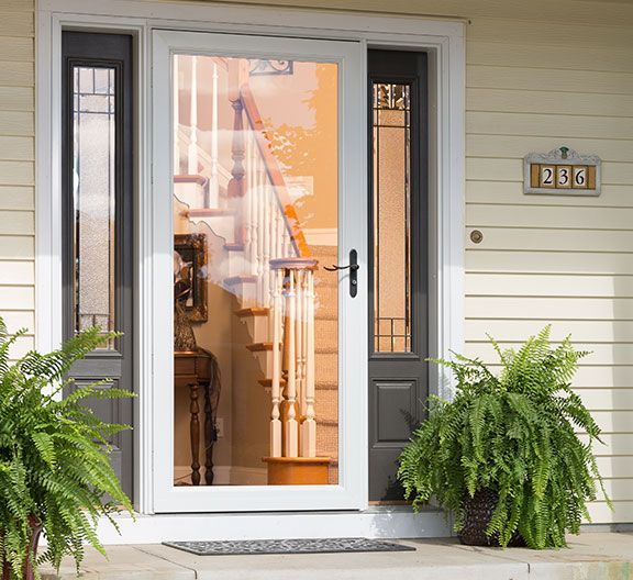 A white storm door with a full glass panel and black handle is flanked by two dark, rectangular side-lite windows.