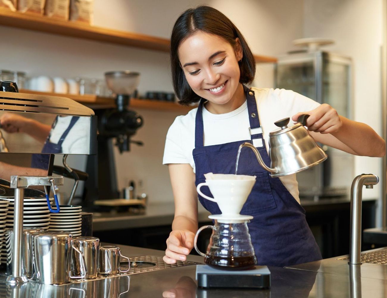 A woman in an apron is pouring coffee into a cup.