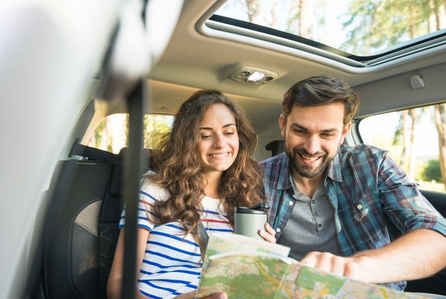 A man and a woman are sitting in the back seat of a car looking at a map.