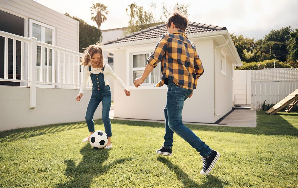 A boy and a girl are playing soccer in a backyard.