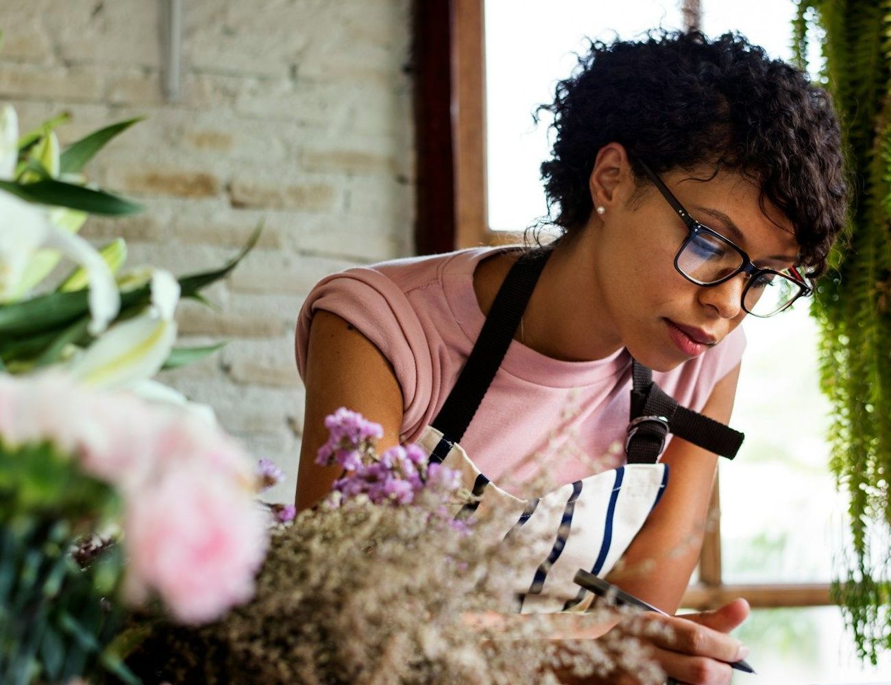 A woman wearing glasses and an apron is working on a flower arrangement.