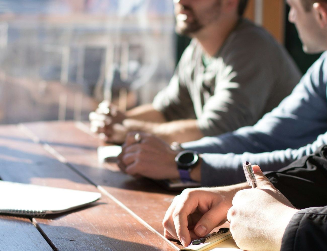 A group of men are sitting at a table writing on a piece of paper.