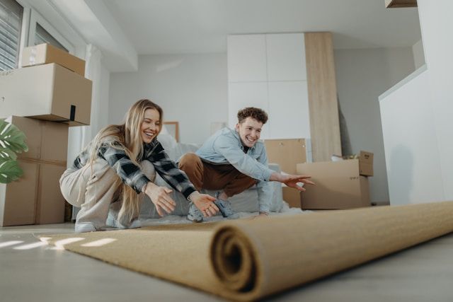 A man and a woman are looking at a roll of carpet in a living room.