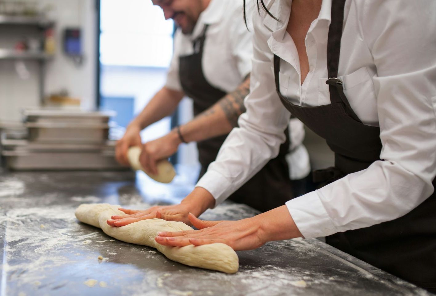 A man and a woman are kneading dough on a counter.