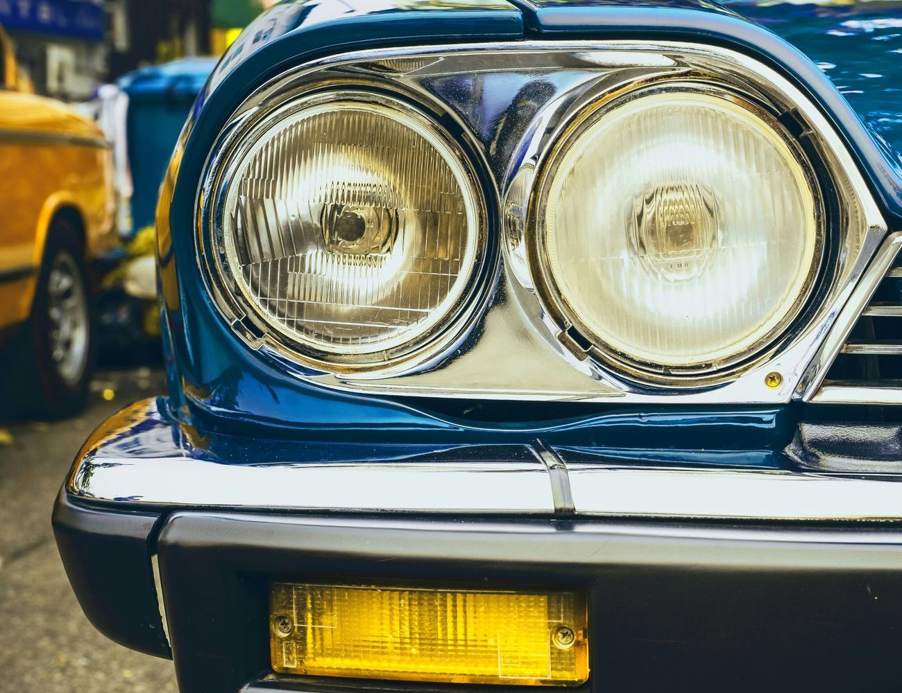 A close up of a blue car with two headlights and a yellow bumper light.