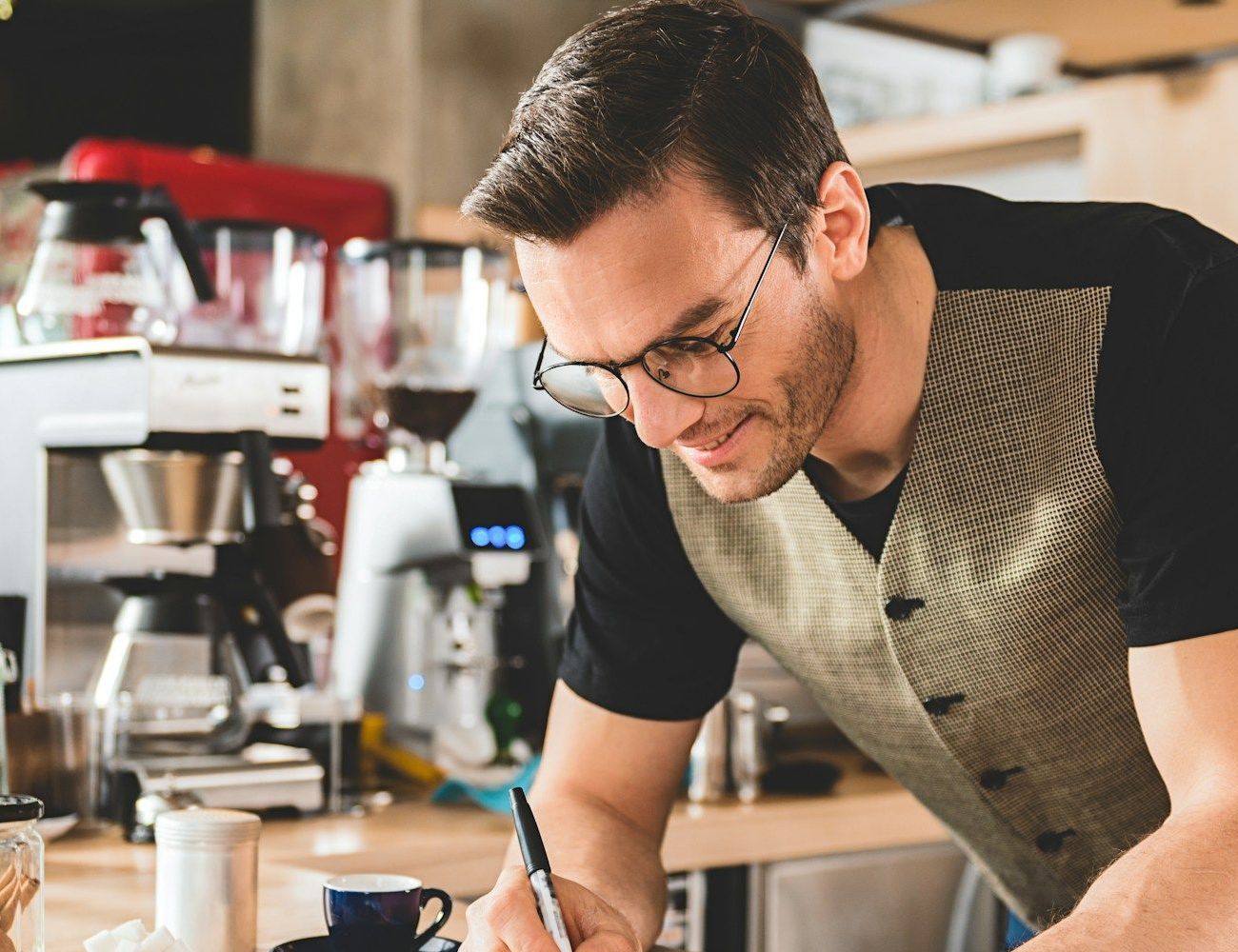 A man wearing glasses is writing on a piece of paper