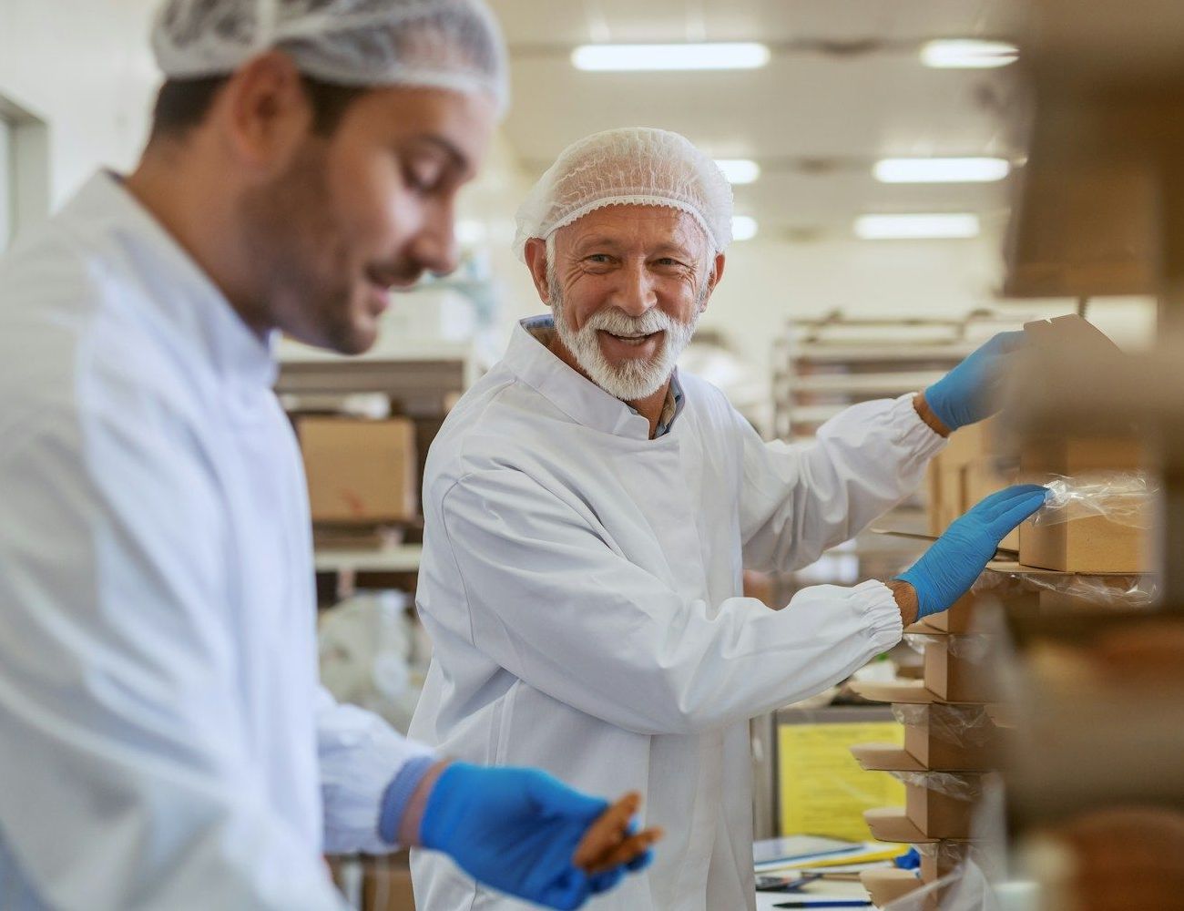 Two men in white coats and blue gloves are working in a factory.