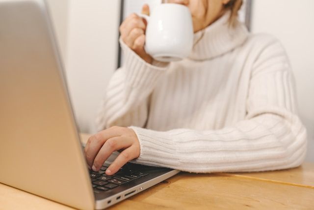 A woman is drinking coffee while using a laptop computer.