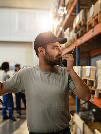 A man is talking on a walkie talkie in a warehouse.