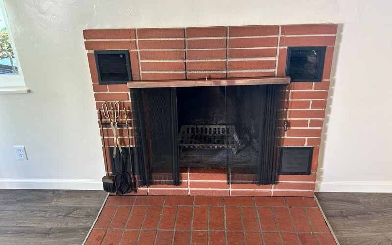 A red brick fireplace with a black screen in a living room.