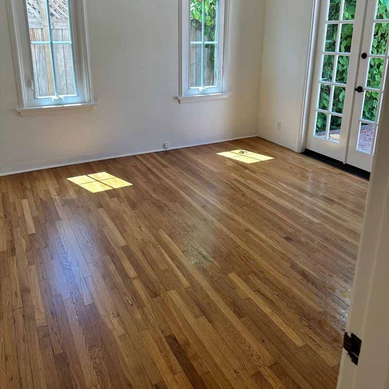 An empty room with hardwood floors and two windows.