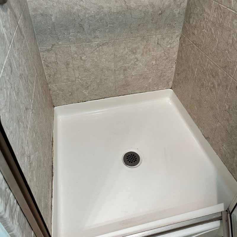 A white shower stall with a drain in a bathroom.