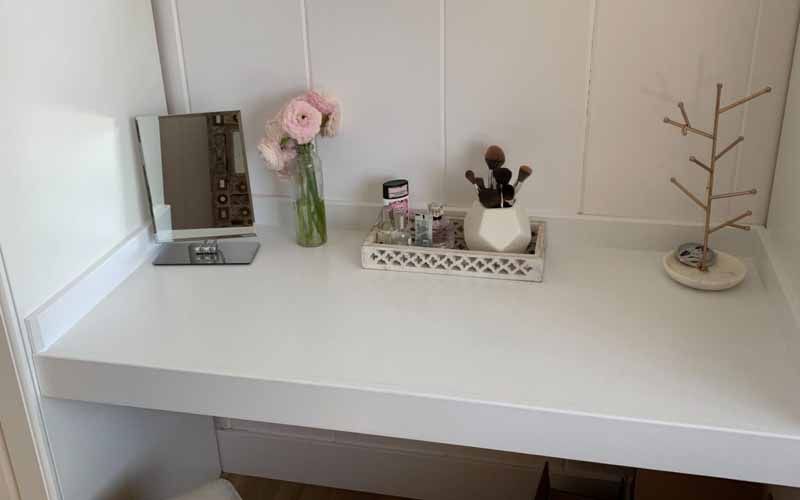 A white vanity with a mirror , brushes , a vase of flowers and a jewelry holder.