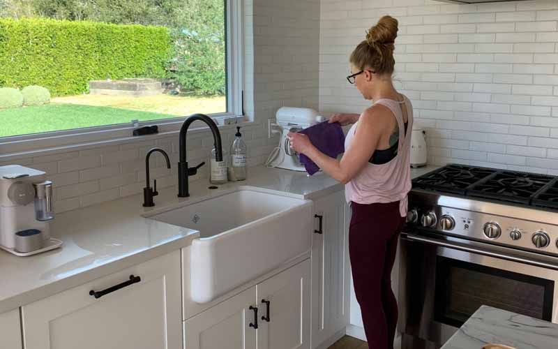 A woman is standing in a kitchen preparing food with a mixer.