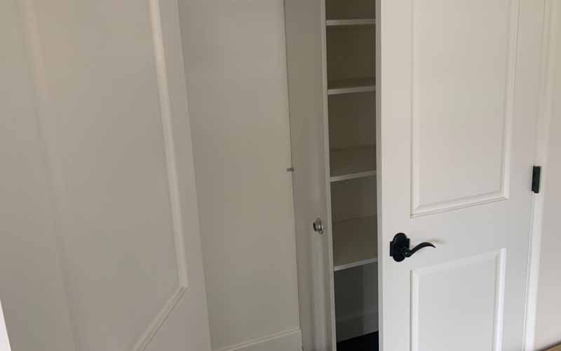 A white door with a black handle is open to a closet with shelves.