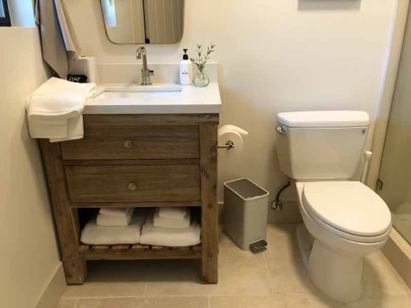 A bathroom with a toilet , sink , mirror and trash can.