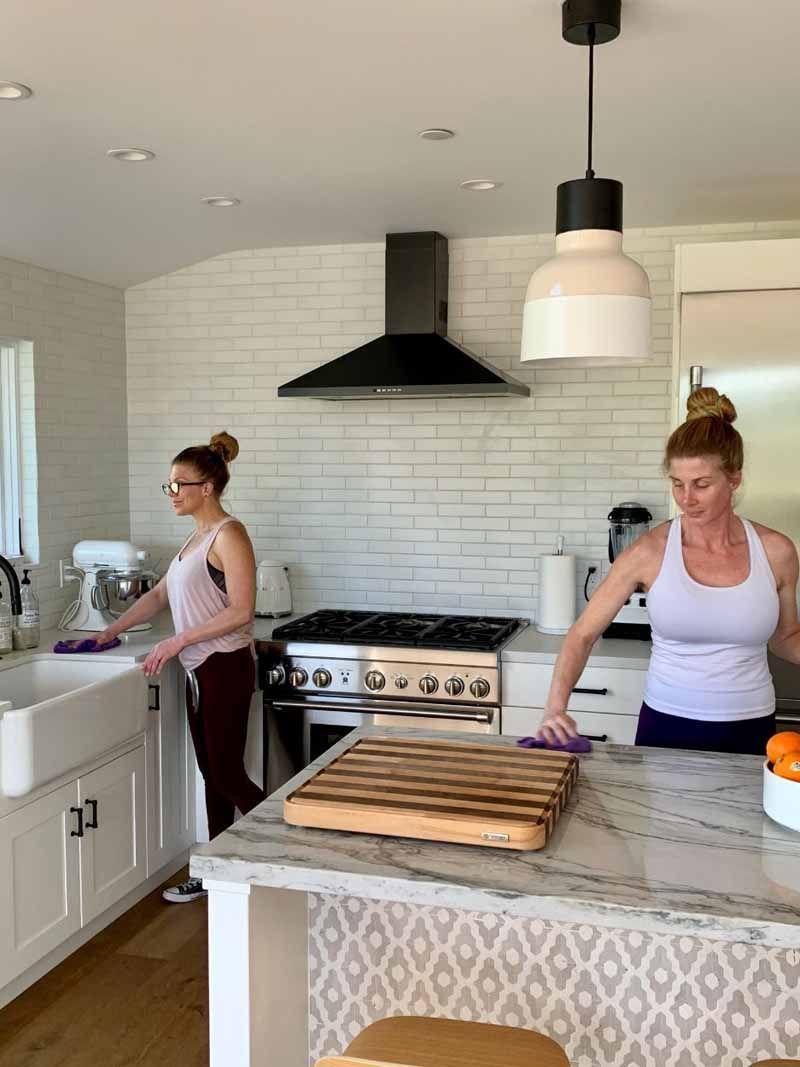 Two women are cleaning a kitchen with a cutting board on the counter