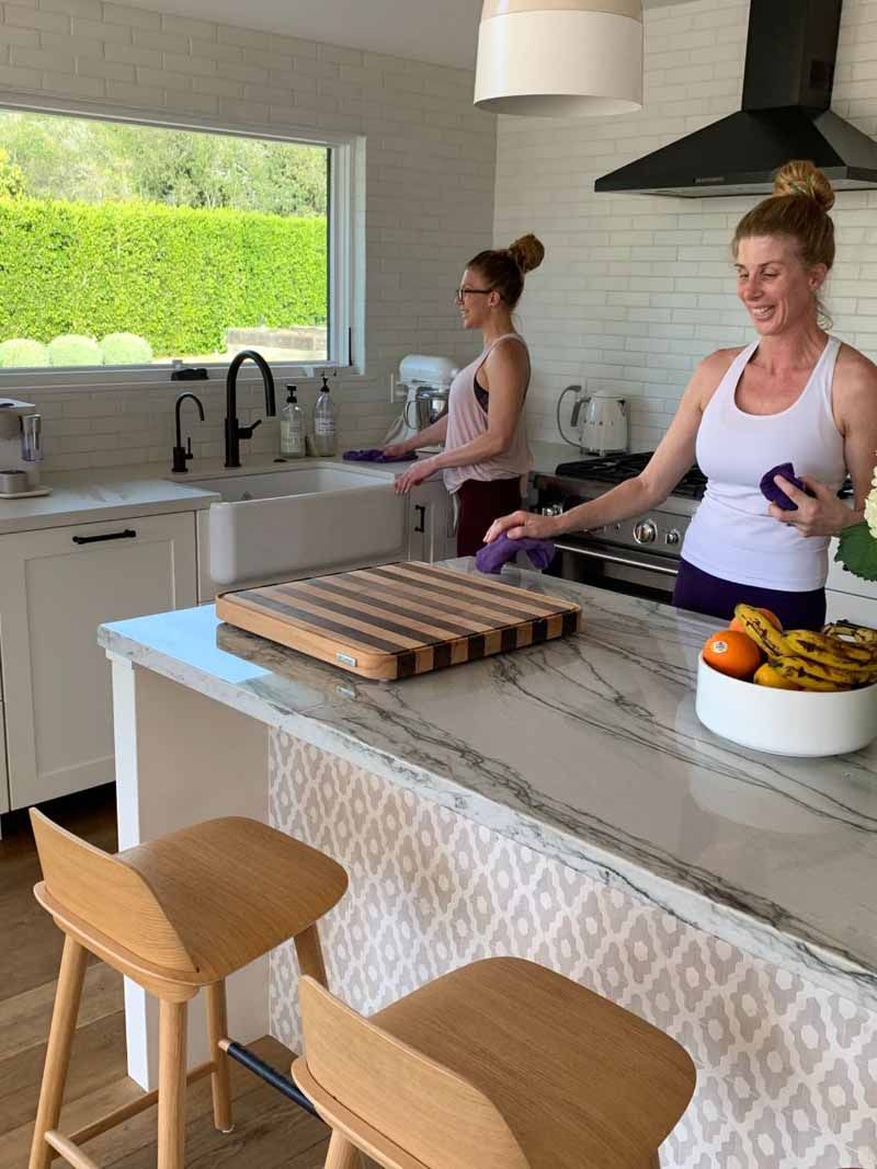 Two women are standing in a kitchen with a cutting board on the counter.