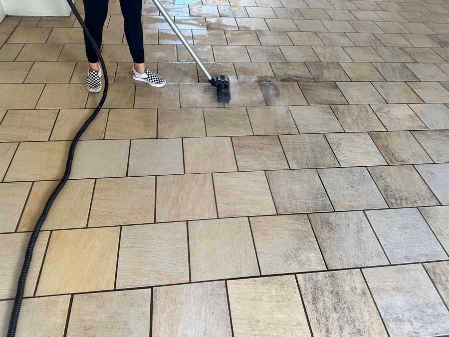 A person is cleaning a tiled floor with a vacuum cleaner.