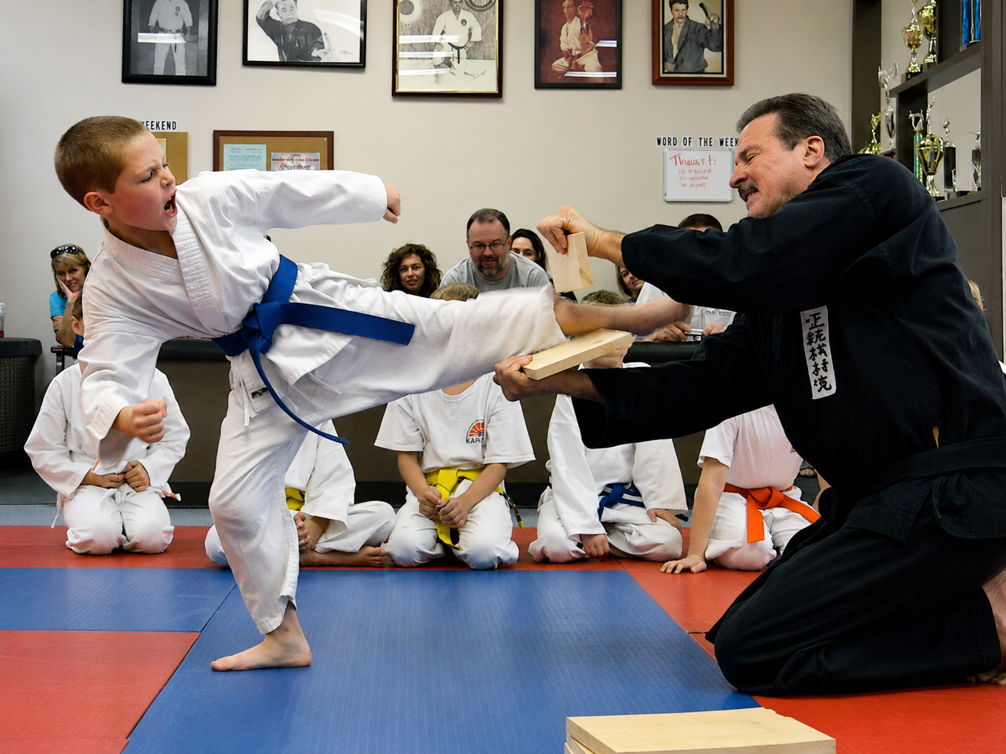 Two men in grappling position on a mat. One embraces the other from behind, both smiling. Gym setting.