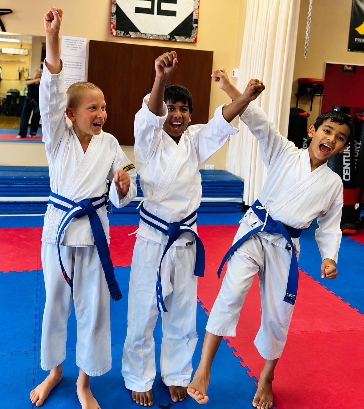 People practicing jiu-jitsu on mats, wearing gis in blue, black, and gray. Active grappling, gym setting.