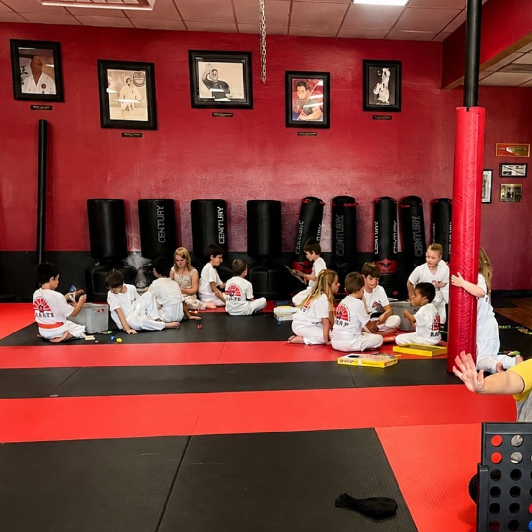 People practicing Brazilian Jiu-Jitsu. One person on the ground, another on top; two others grappling nearby. Black gis, indoor setting.