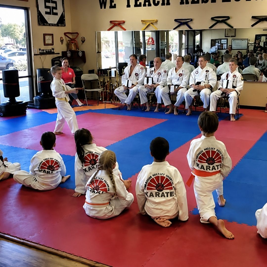 Two young children in blue and black martial arts uniforms grappling on a gym floor, one smiling.