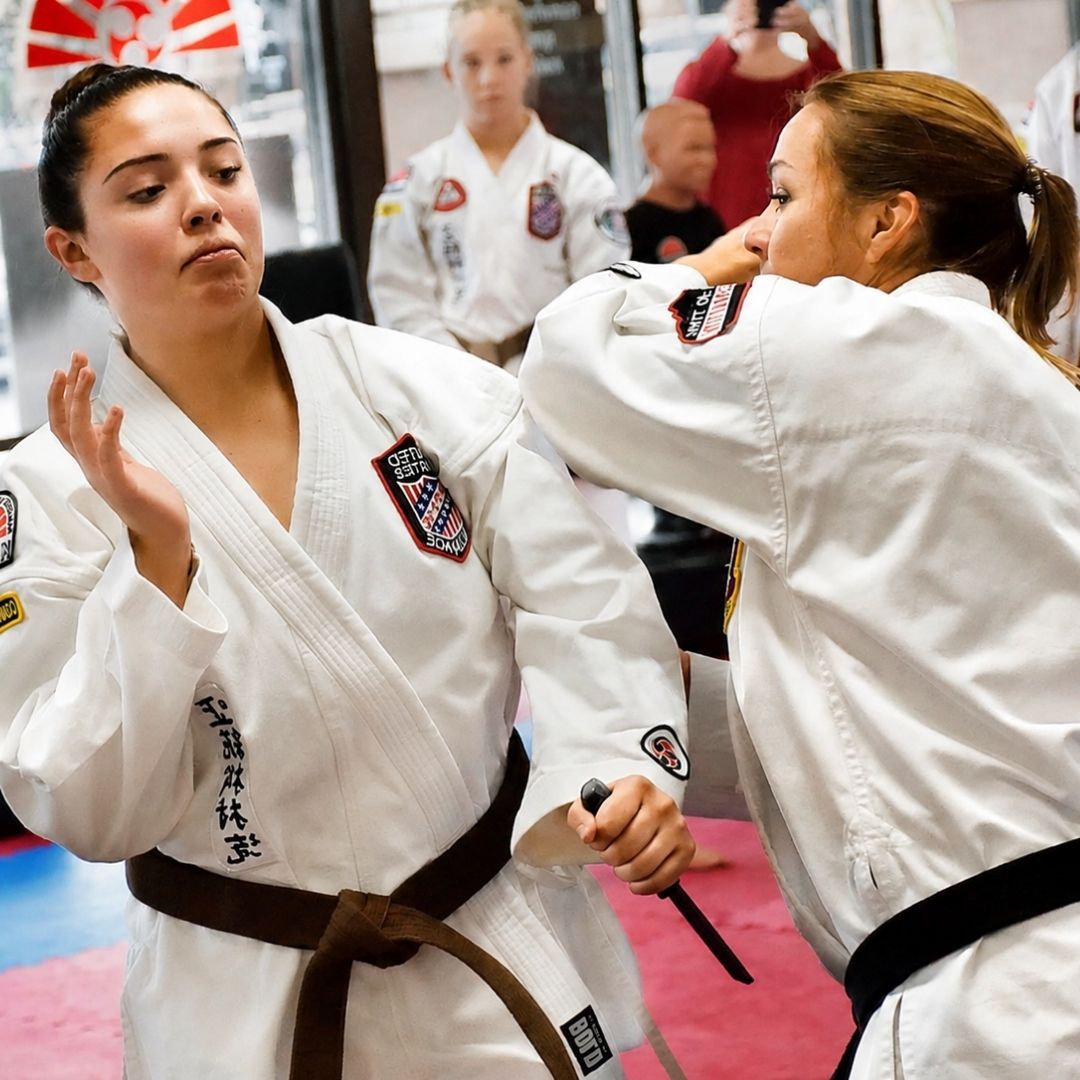Two people practicing Brazilian Jiu-Jitsu on a mat; one in a black gi, one in a white gi, grappling.
