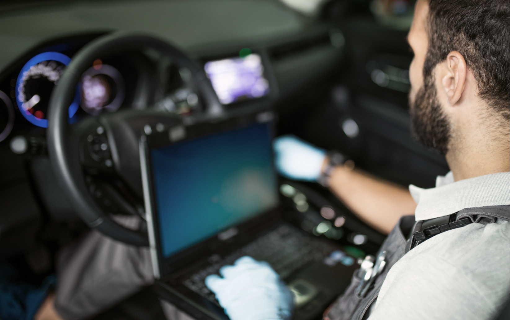 A man is sitting in a car using a laptop computer.