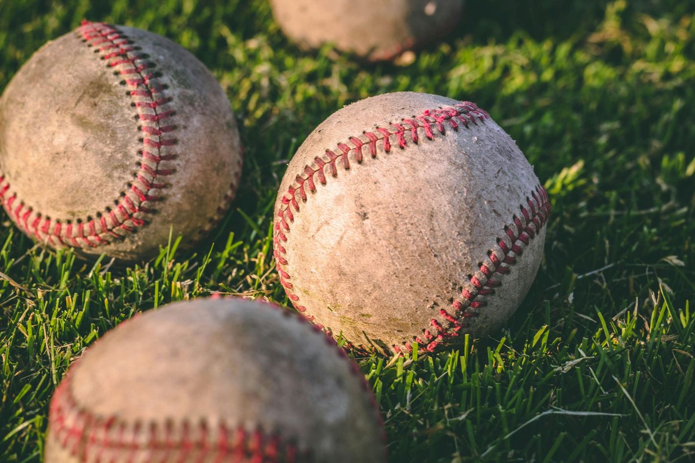 Three worn baseballs resting on green grass in sunlight