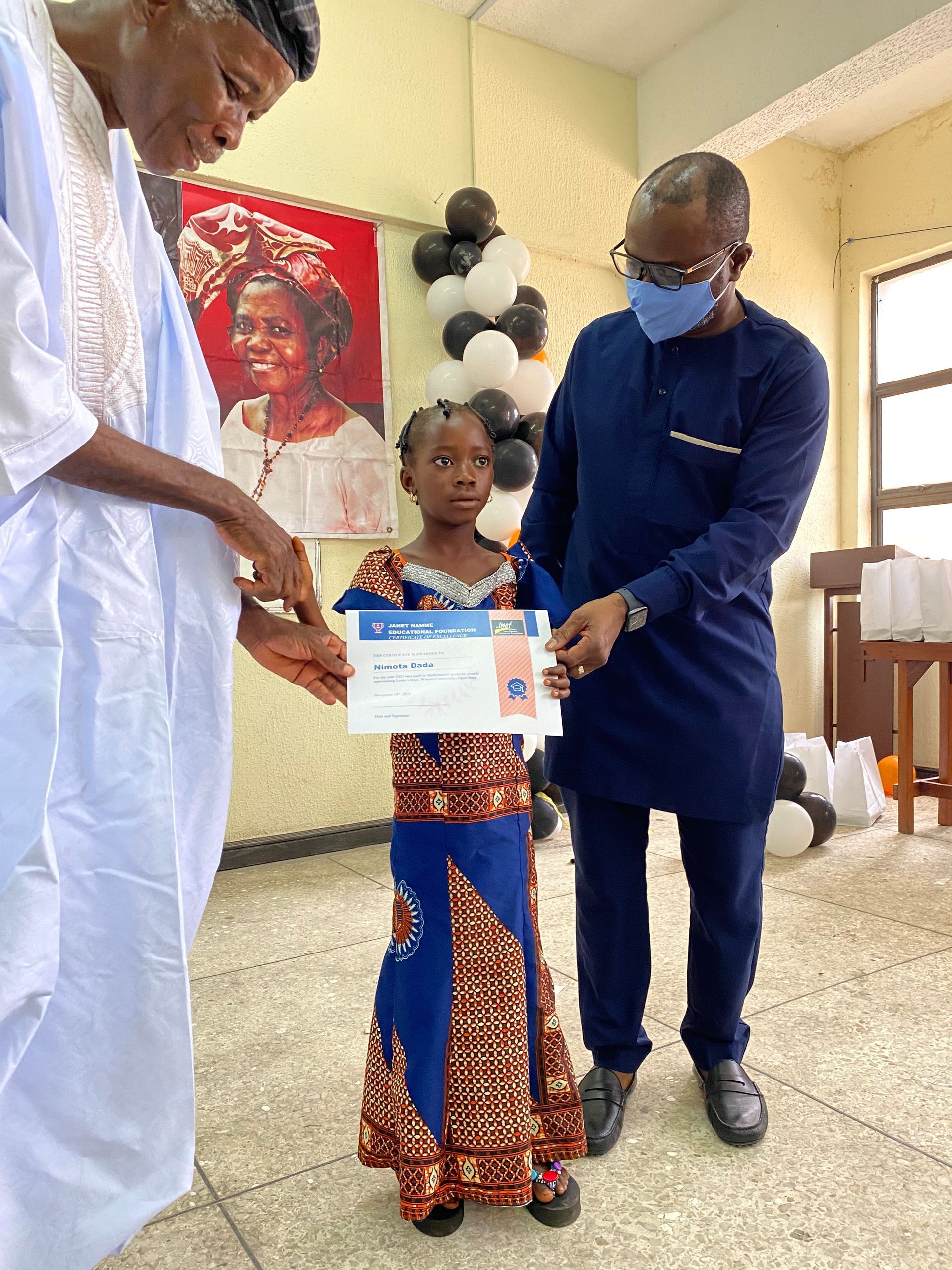 Two men are standing next to a little girl holding a certificate.