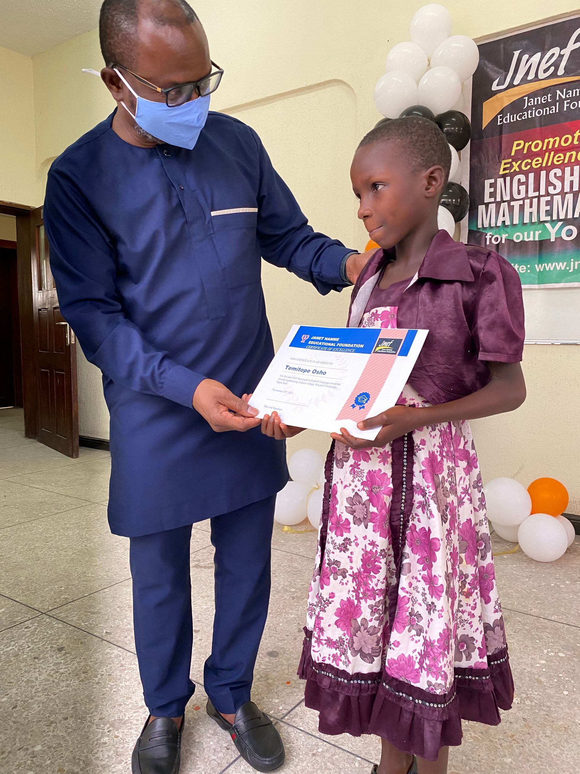 A man wearing a mask is giving a certificate to a little girl.