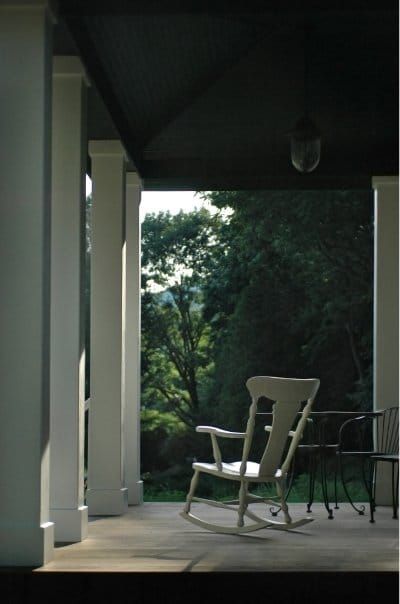 A rocking chair sits on a porch with trees in the background
