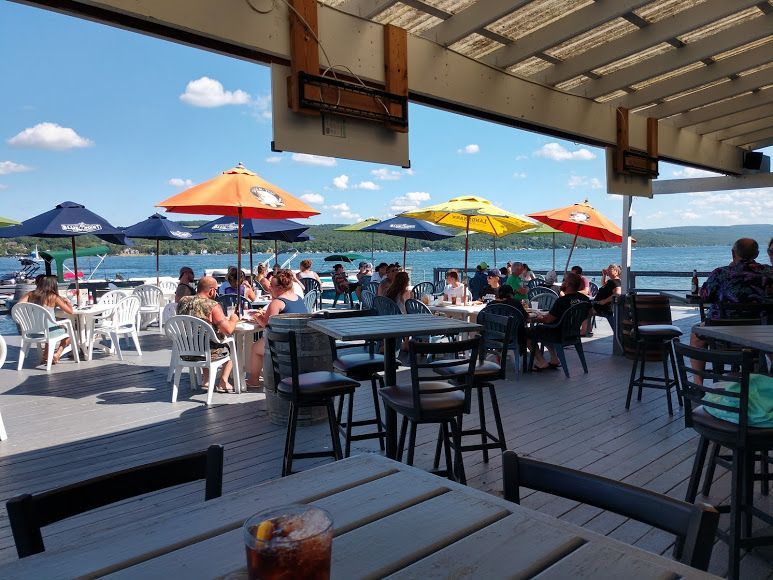 A group of people are sitting at tables on a deck overlooking a lake.