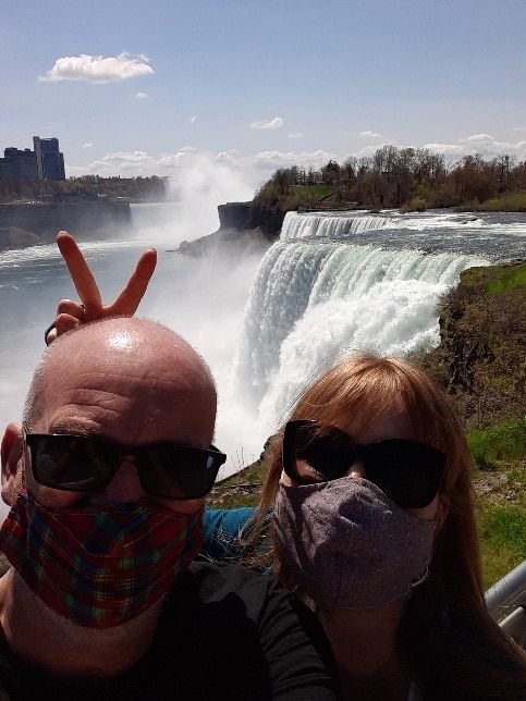 A man and a woman wearing face masks are posing for a picture in front of a waterfall.