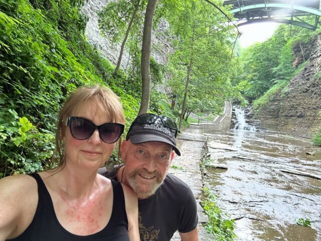 A man and a woman are taking a selfie in front of a waterfall.