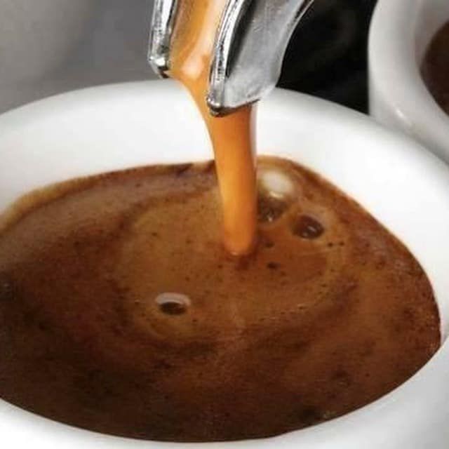 A close up of a cup of coffee being poured into it.