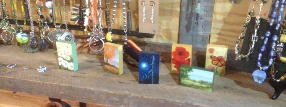 A display of jewelry and paintings on a wooden table.