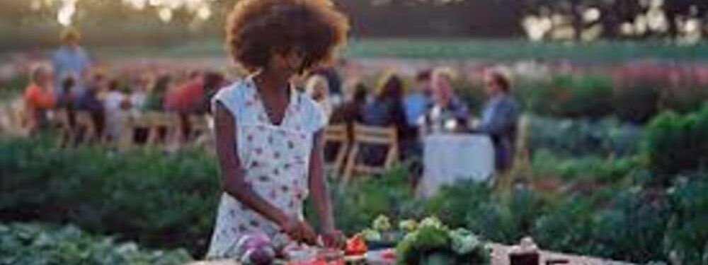 A woman is standing in front of a table cutting vegetables.