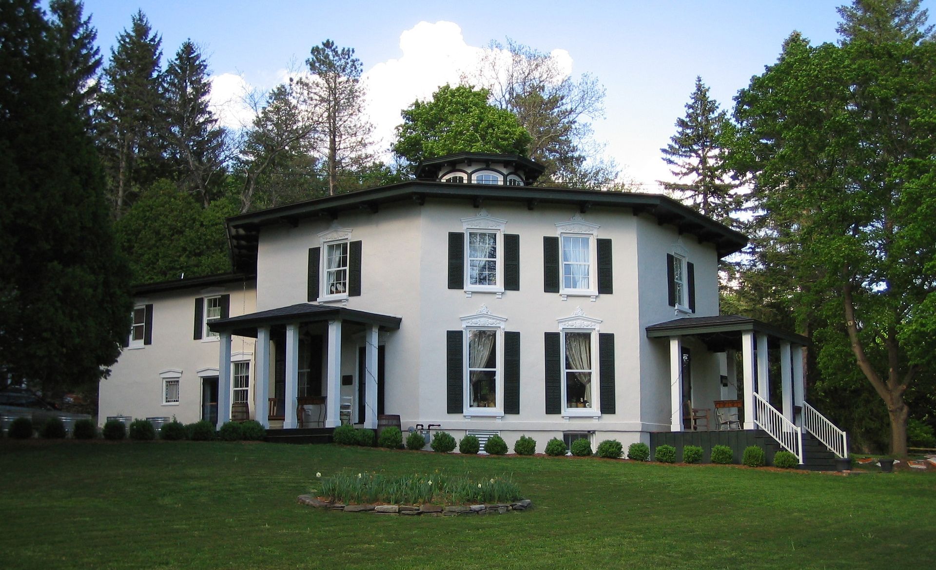 A large white house with black shutters is surrounded by trees