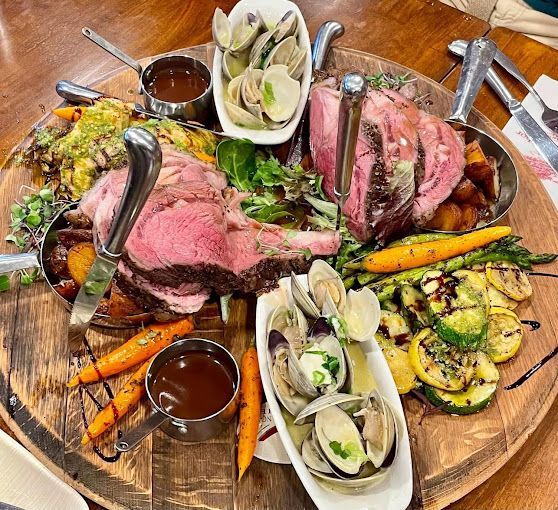 A wooden cutting board topped with meat and vegetables on a table.