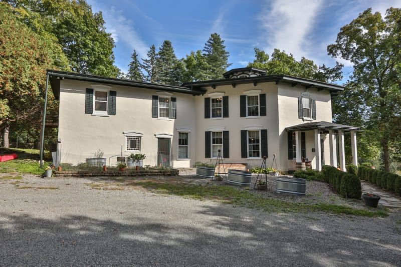 A large white house with black shutters is surrounded by trees.