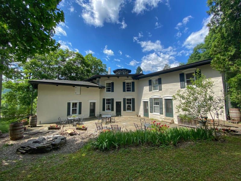 A large white house with a patio in front of it surrounded by trees.