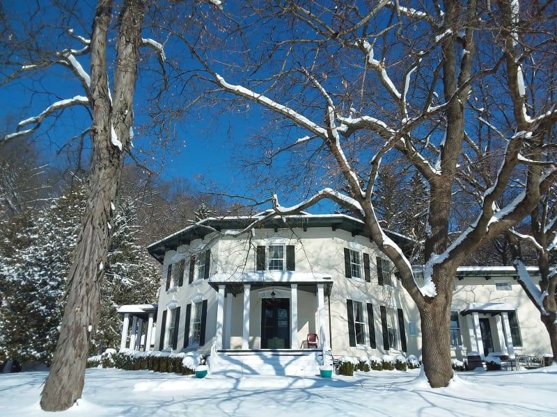 A large white house is surrounded by snow covered trees
