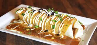 A burrito is sitting on a white plate on a wooden table.