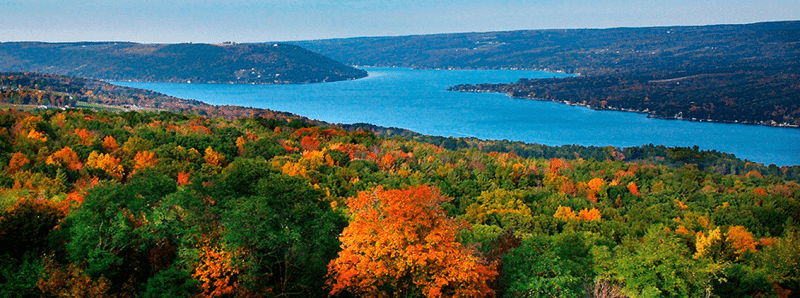 Panoramic view of a lake bordered by fall foliage in shades of green, yellow, and orange.