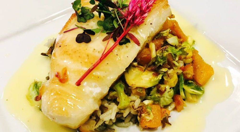 A white plate topped with a piece of fish and vegetables.