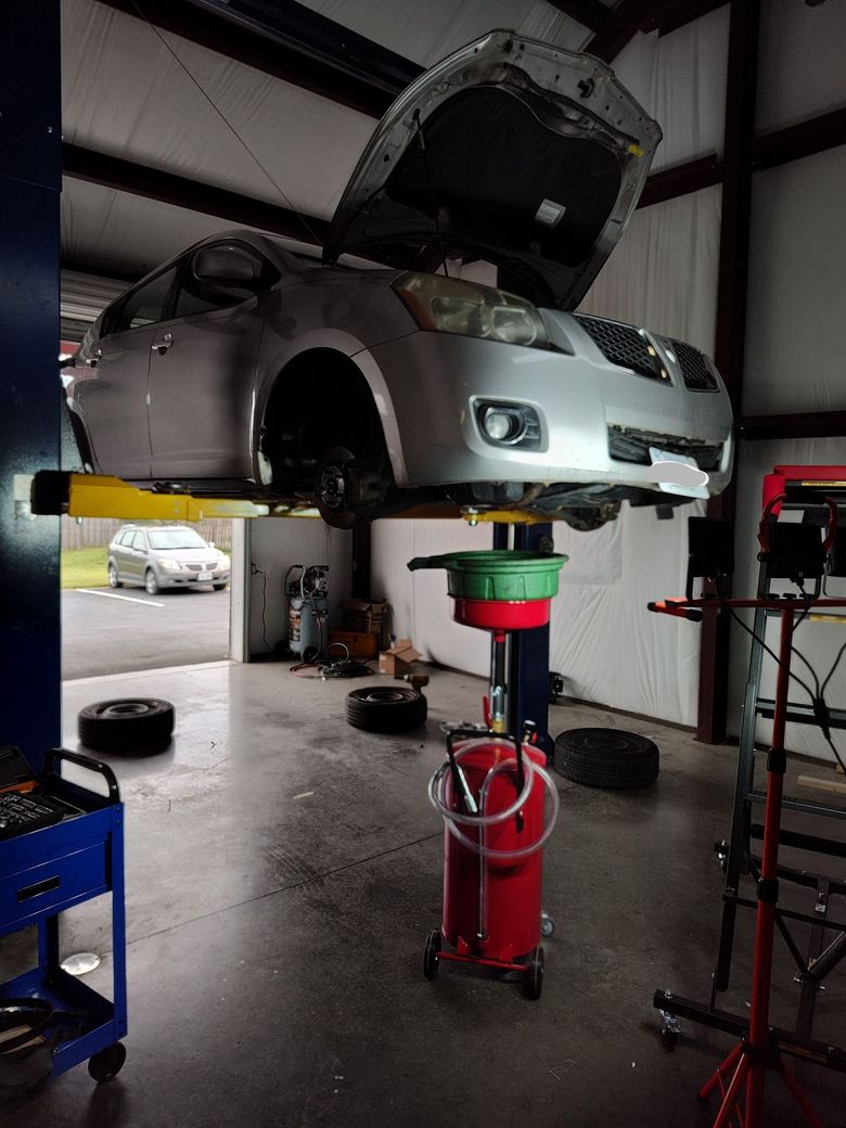 Mechanic working under an open car hood in a bright auto repair shop Mechanic working under an open car hood in a bright auto repair shop